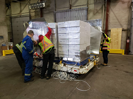Staff load boxes of chilled pork onto PMC aircraft pallets under CFIA supervision at Edmonton International Airport