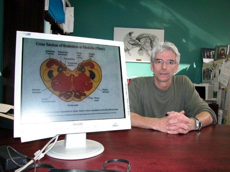 Dr Yves Robinson en retrait, l'écran d'ordinateur affiche l'image d'un cerveau de vache présentant des lésions.