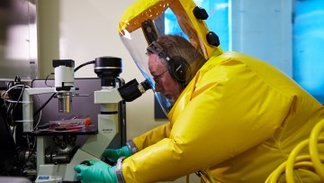 A scientist in a biohazard suit looks into a microscope in a laboratory at the National Centre for Foreign Animal Disease