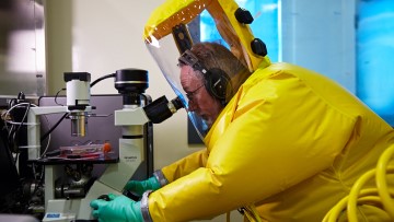 Un scientifique en combinaison de protection biologique utilise un microscope dans un laboratoire du Centre national des maladies animales exotiques