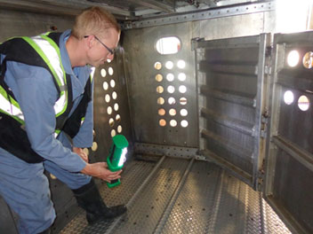A wash station employee wearing clean coverall and footwear to inspect a transport unit.