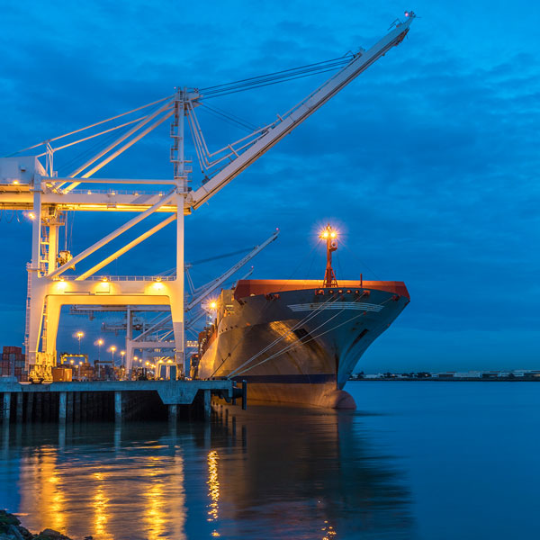 A cargo ship is in a port preparing to dock. There is a crane on the dock.