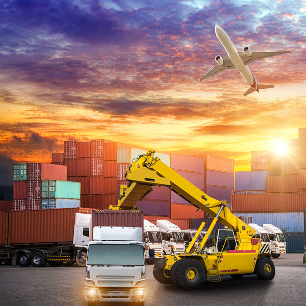A plane flying in the sky. Below the plane there are forklifts placing shipping containers onto  transport trucks.